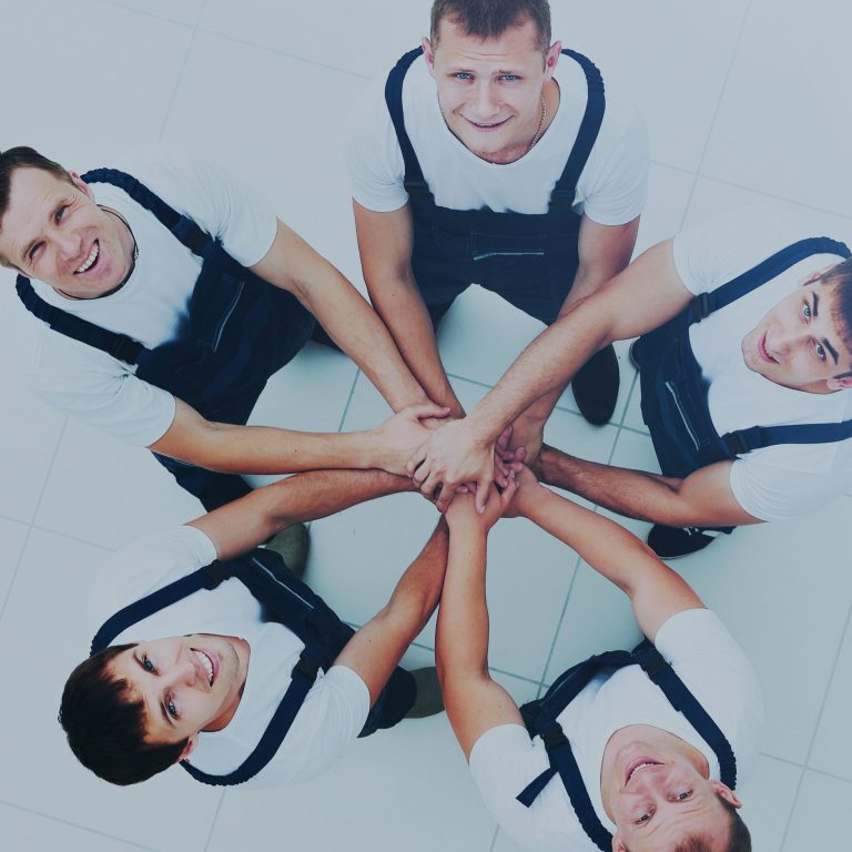 Cinq hommes en salopettes blanches se tenant par les mains en formant un cercle.