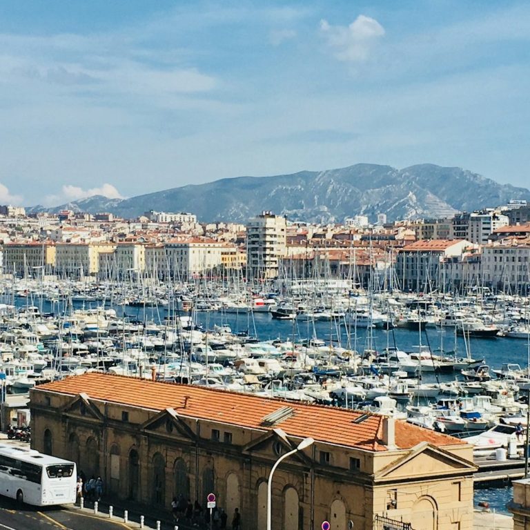 Vue du port de Marseille, avec des bateaux et des montagnes en arrière-plan.