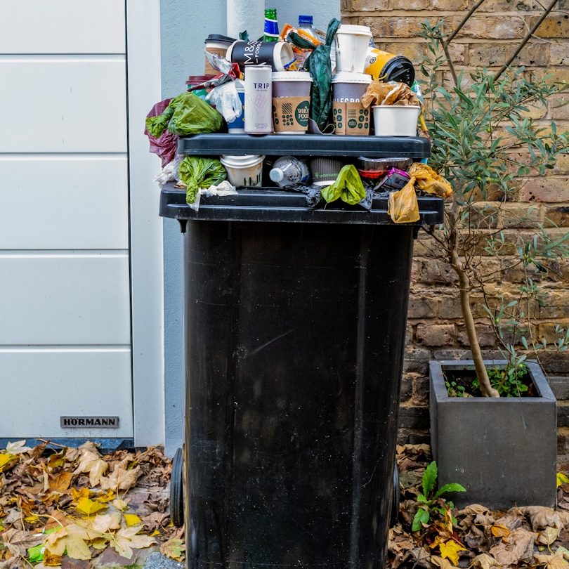 Une poubelle débordante de déchets variés, avec des bouteilles et des gobelets.