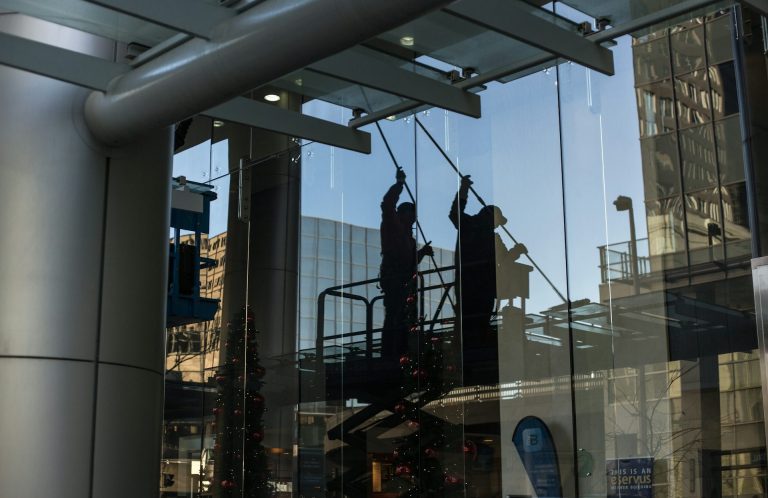 Deux travailleurs sont en intervention dans un bâtiment, reflétant l'environnement urbain.