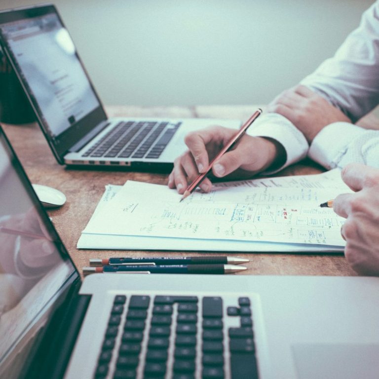 Main dans une prise de notes avec un ordinateur portable et des documents sur une table.