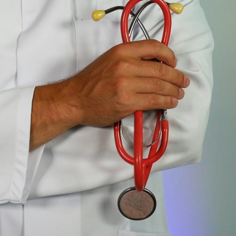 Personne tenant un stéthoscope rouge, vêtu d'une blouse blanche.