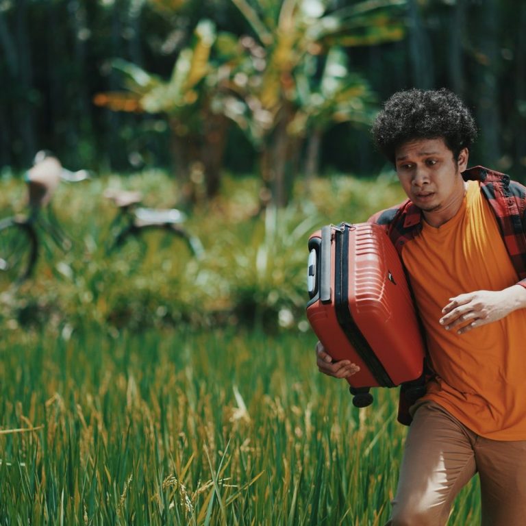 Un homme avec une valise rouge cours à travers un champ de riz verdoyant.