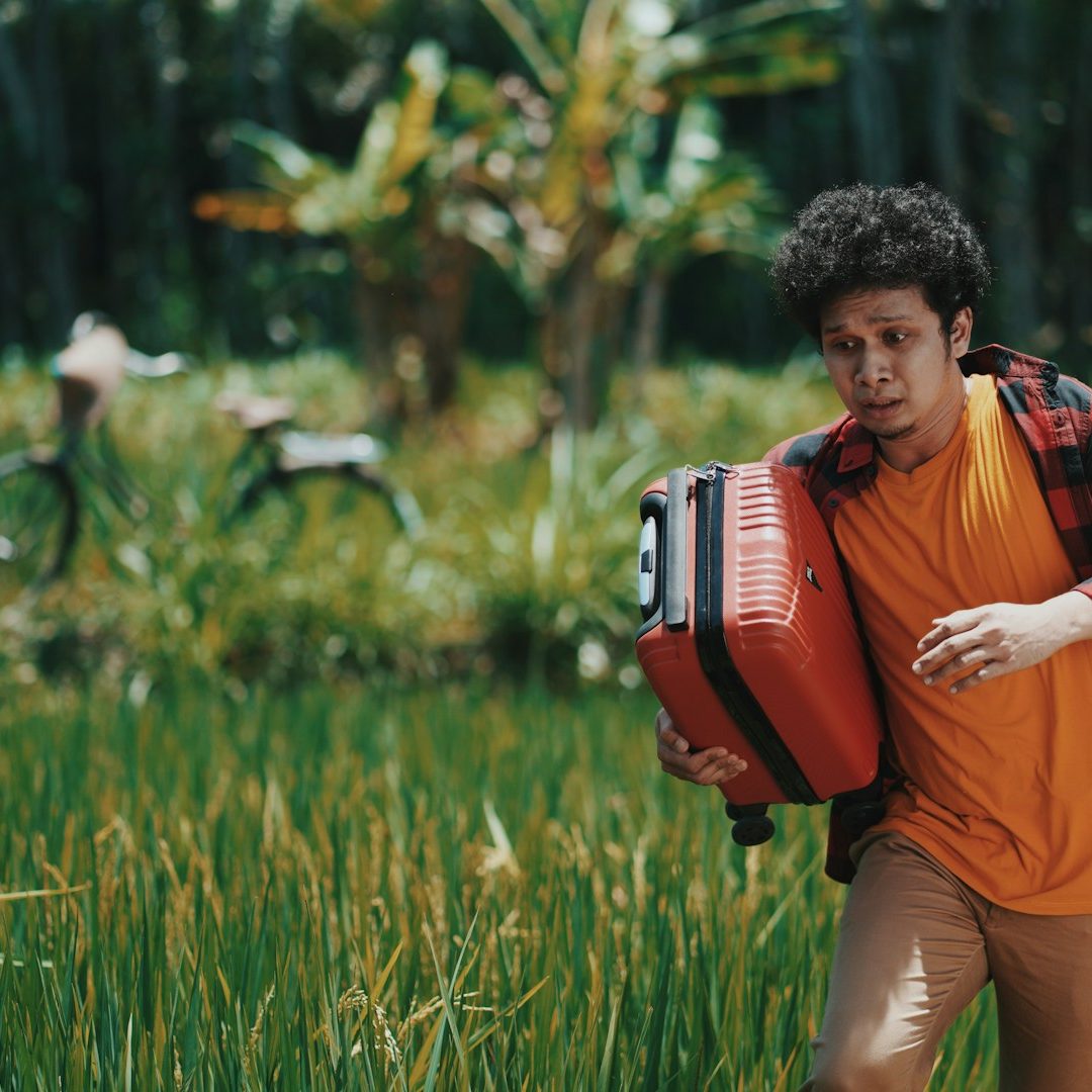 Un homme avec une valise rouge cours à travers un champ de riz verdoyant.